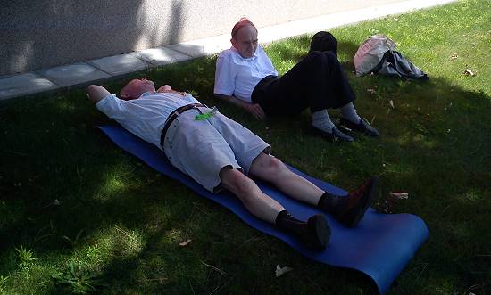 zwei ältere Chorfahrtteilnehmer auf Iso-Matten im Gebäudeschatten